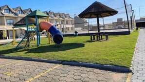 A playground with a slide and climbing structure, surrounded by a fenced area with benches and a covered seating area. - Houses in a Beachfront Condominium With a Swimming Pool in Itajuba - Mcss (Barra Velha)