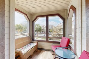 A covered balcony with wicker furniture, a glass table, and a view of residential buildings. - Cozy Cabin with 4 bed/3.5 bath- hot tub, pool, firepit, views & Central AC (Myrtle Beach)