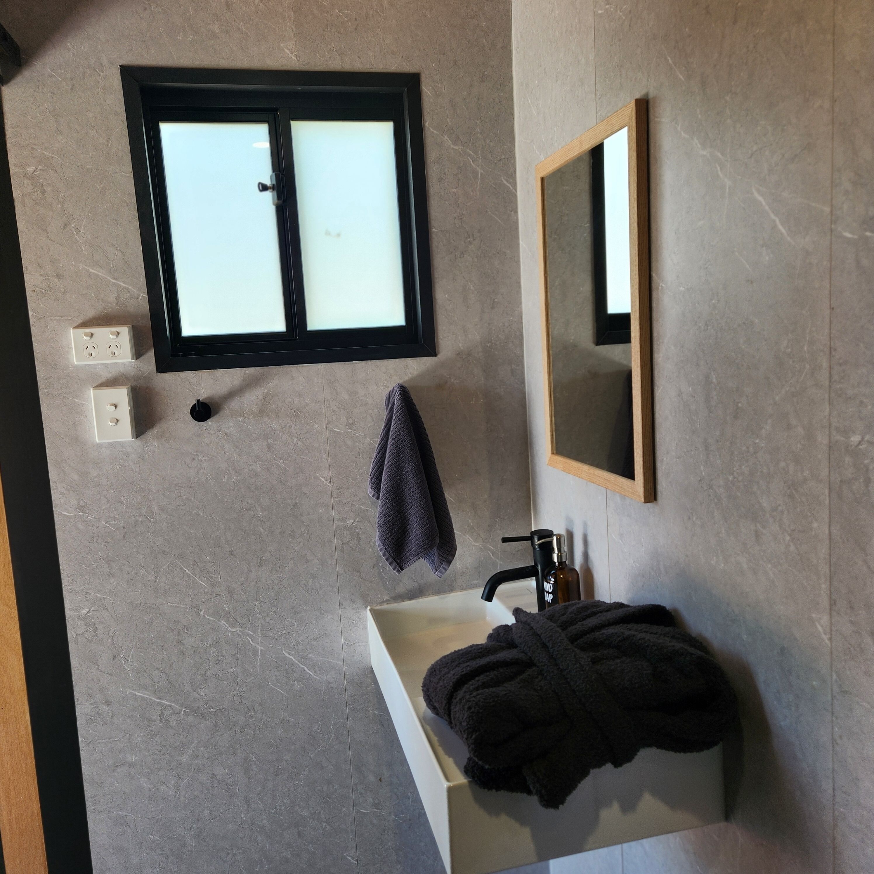 A bathroom with a window, a sink, a mirror, and a towel rack.