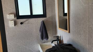 A bathroom with a window, a sink, a mirror, and a towel rack.