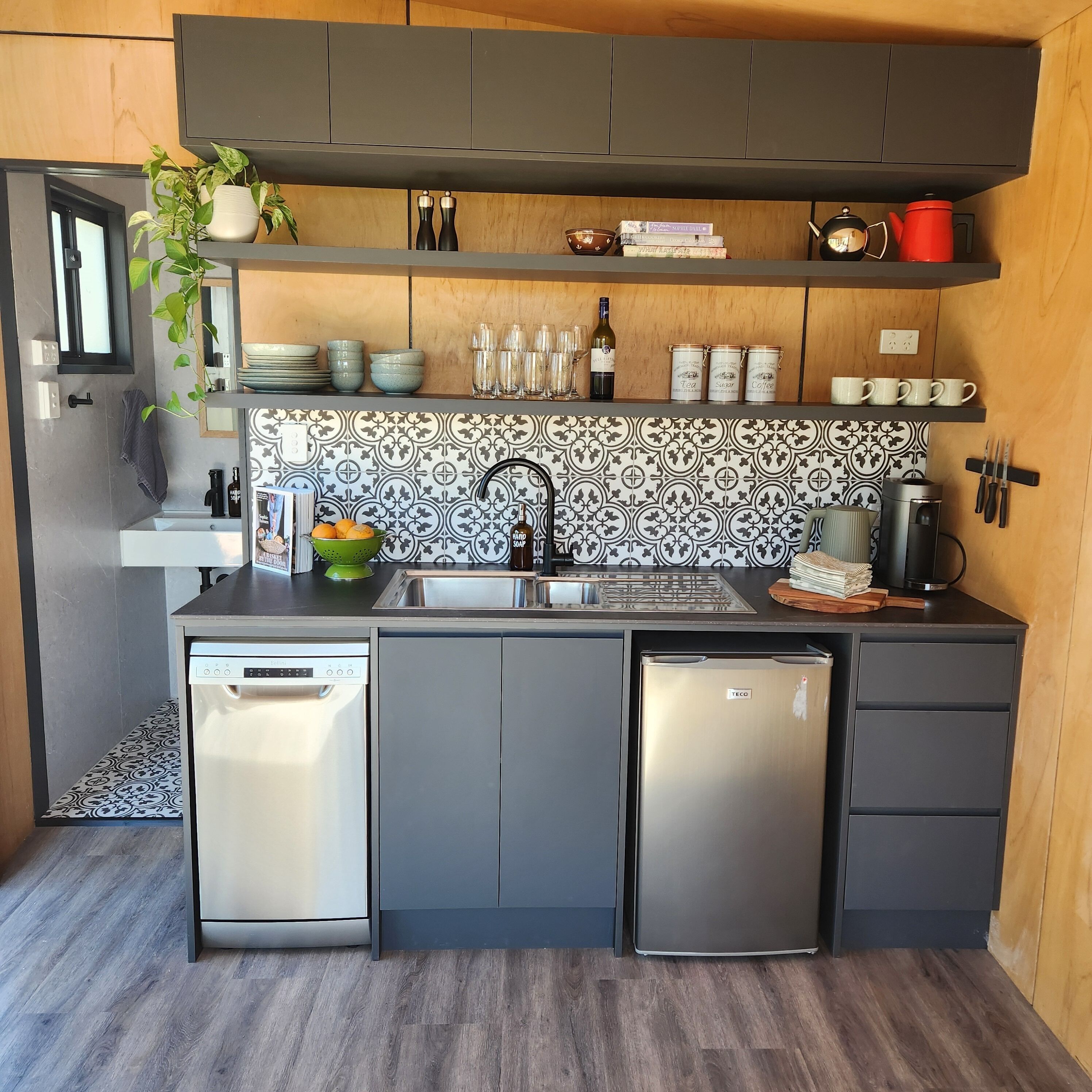 A modern kitchen with grey cabinets, a black backsplash, and stainless steel appliances.