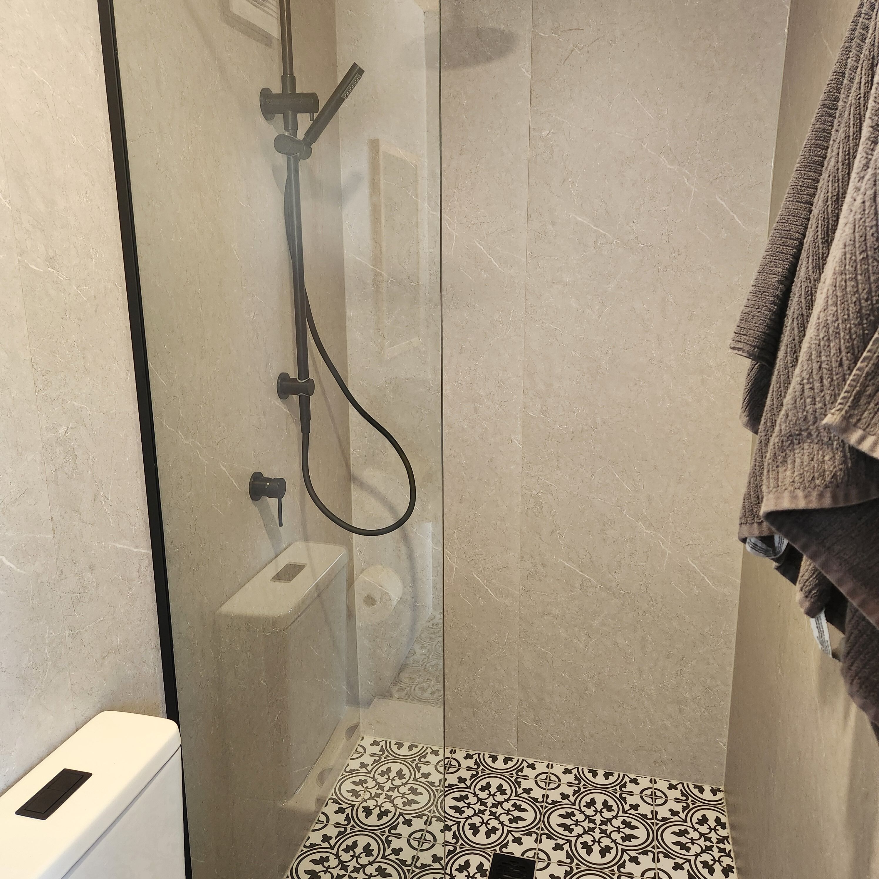 A glass-enclosed shower with a handheld showerhead, a handheld shower head, and a wall-mounted faucet.