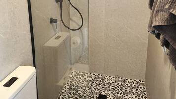 A glass-enclosed shower with a handheld showerhead, a handheld shower head, and a wall-mounted faucet.
