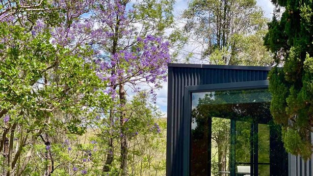 Eine moderne Holzhütte mit großem Fenster, einer Holzterrasse und einer weißen Badewanne.