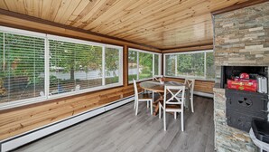 A dining area with a wooden ceiling, large windows, and a stone fireplace.