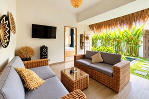 A modern living room with a grey sofa, a wicker coffee table, and a television mounted on the wall.