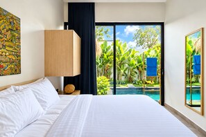 Une chambre d’hôtel avec un grand lit, une table de chevet, une lampe, une vue sur une piscine et des plantes tropicales.