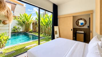 A bedroom with a large bed, a bathroom with a sink, and a view of a swimming pool with tropical plants.