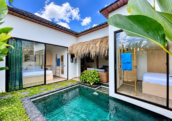 Una villa moderna con piscina, puertas de cristal y techo de paja.