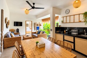 A modern living space with a dining area, kitchen, and a large window with a view of greenery. - Canggu Bohemian Villa | Private Pool & Rice Views (Kancil)