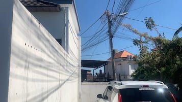 Ein weißes Auto steht in einer schmalen Auffahrt vor einem Haus mit rotem Ziegeldach.