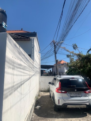 A white car parked in a narrow driveway with a red-tiled roof house in the background. - Canggu Bohemian Villa | Private Pool & Rice Views (Kancil)