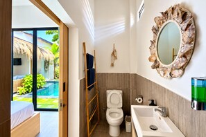 Un baño moderno con inodoro, lavamanos y espejo con marco en forma de hoja.
