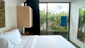 A hotel room with a bed, a large window, a view of a garden, and a blue chair outside. - Boutique Bohemian Villa in Canggu's Heart. (Kancil)