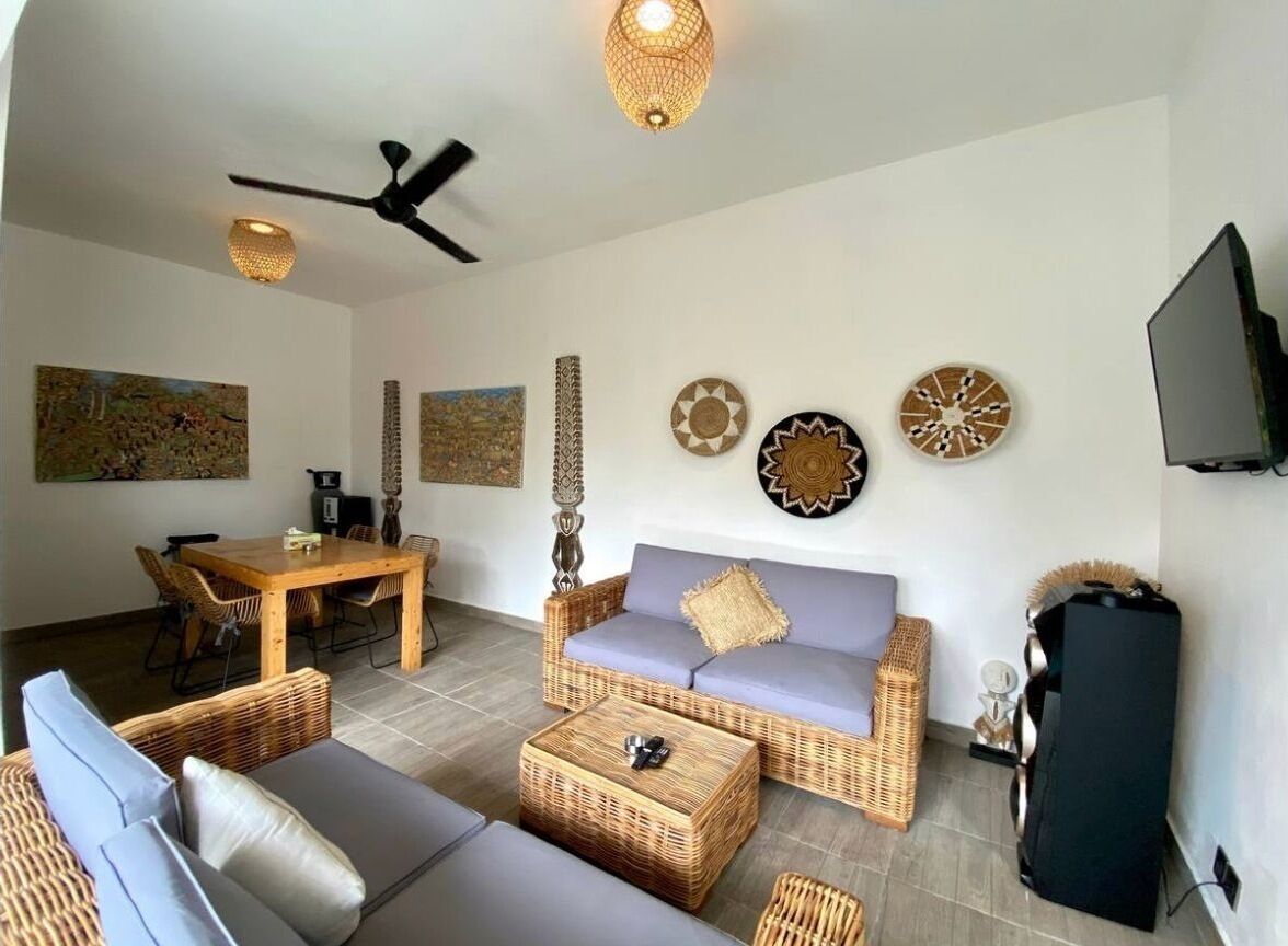 Una sala de estar con muebles de mimbre, ventilador de techo, cuadros en la pared y televisor.