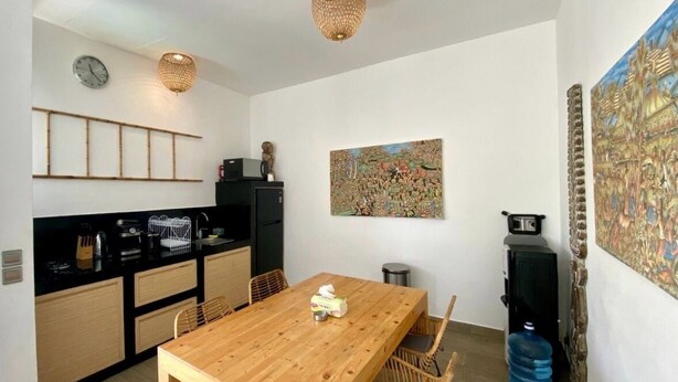 A modern kitchen with a wooden table and chairs, a black countertop, and a large water dispenser. - Boutique Bohemian Villa in Canggu's Heart. (Kancil)
