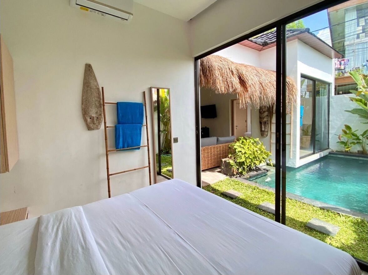 Un dormitorio con una cama grande, vista a una piscina y una estructura de techo de paja en el exterior.