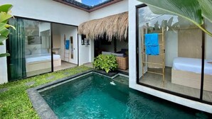 A modern villa with a swimming pool, glass doors leading to a bedroom, and a thatched roof. - Boutique Bohemian Villa in Canggu's Heart. (Kancil)