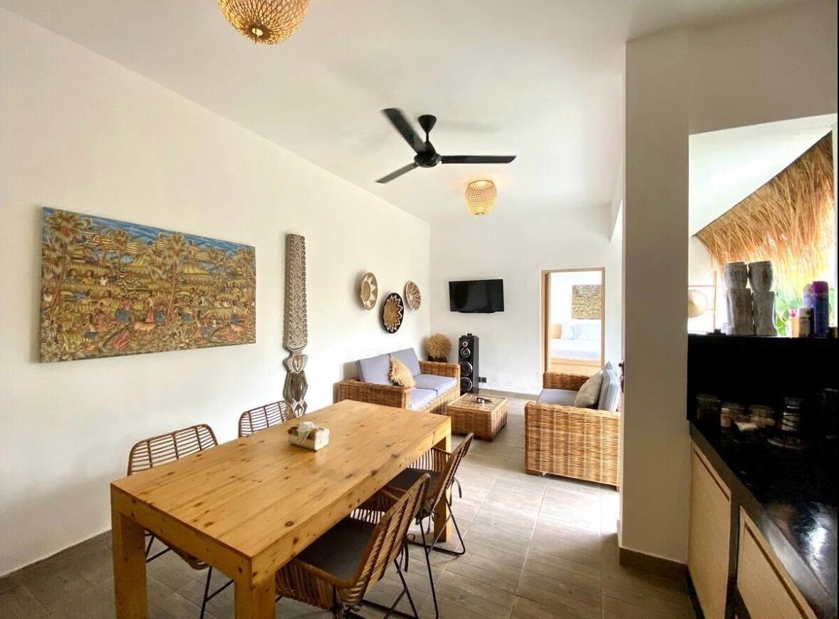 Un amplio salón con una mesa de comedor de madera, muebles de mimbre y un ventilador de techo.