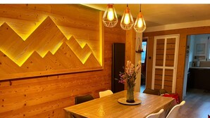 A wooden dining area with a table and chairs, a decorative wall with a geometric pattern, and pendant lighting. - Christmas Apt | Parking + Balcony | Near Center (Morzine)