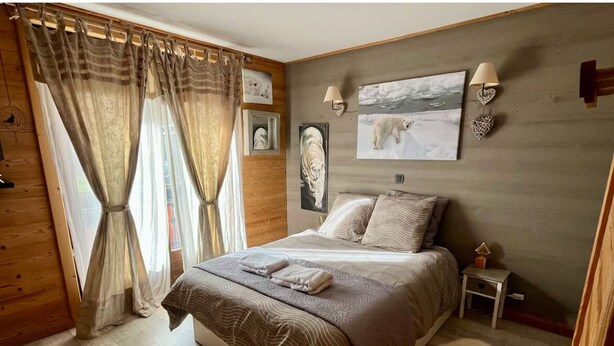 A bedroom with a large bed, wooden walls, a small bedside table, and a polar bear picture on the wall. - Christmas Apt | Parking + Balcony | Near Center (Morzine)