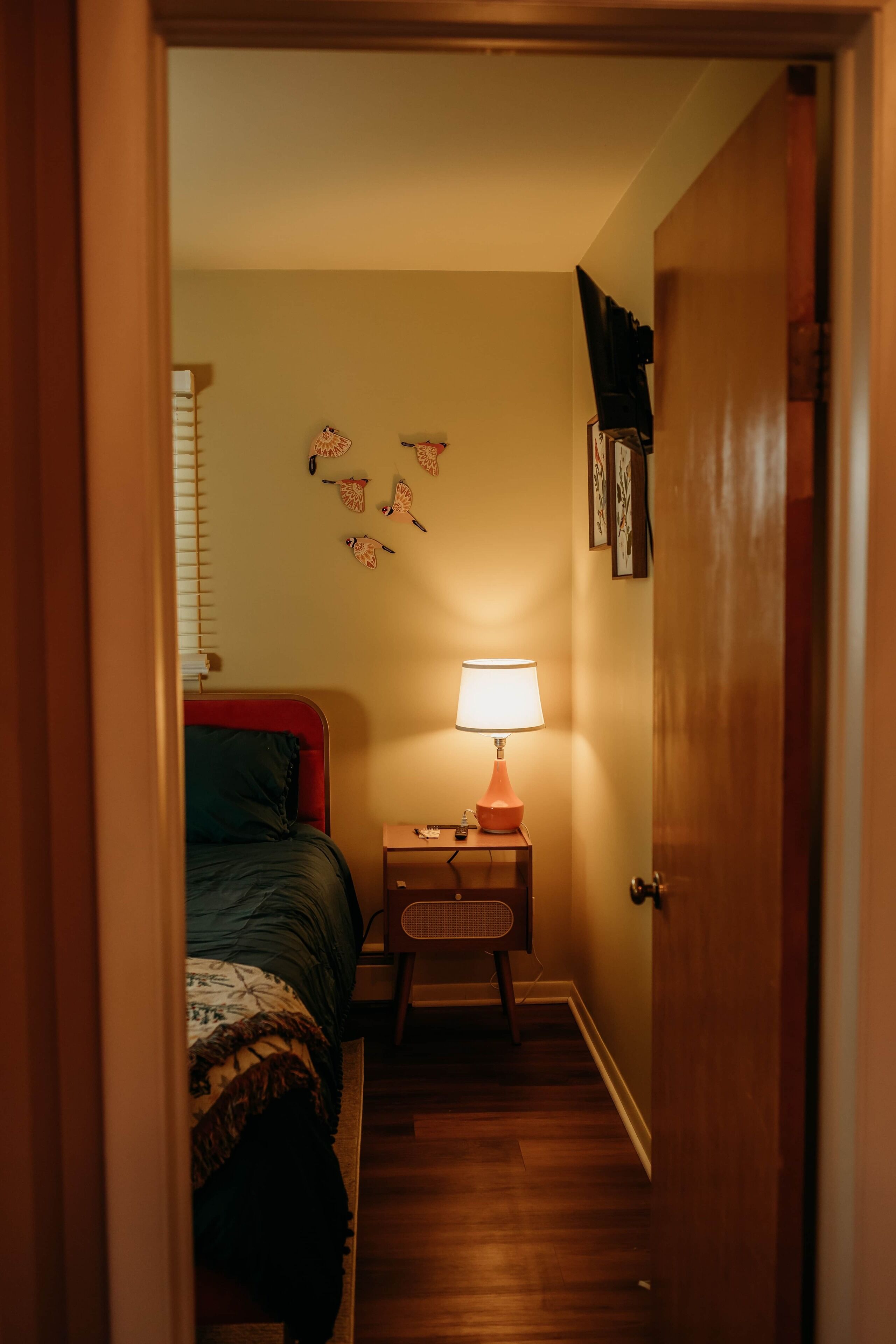 Un corridoio stretto che conduce a una camera da letto, con un letto, un comodino con una lampada e decorazioni alle pareti.