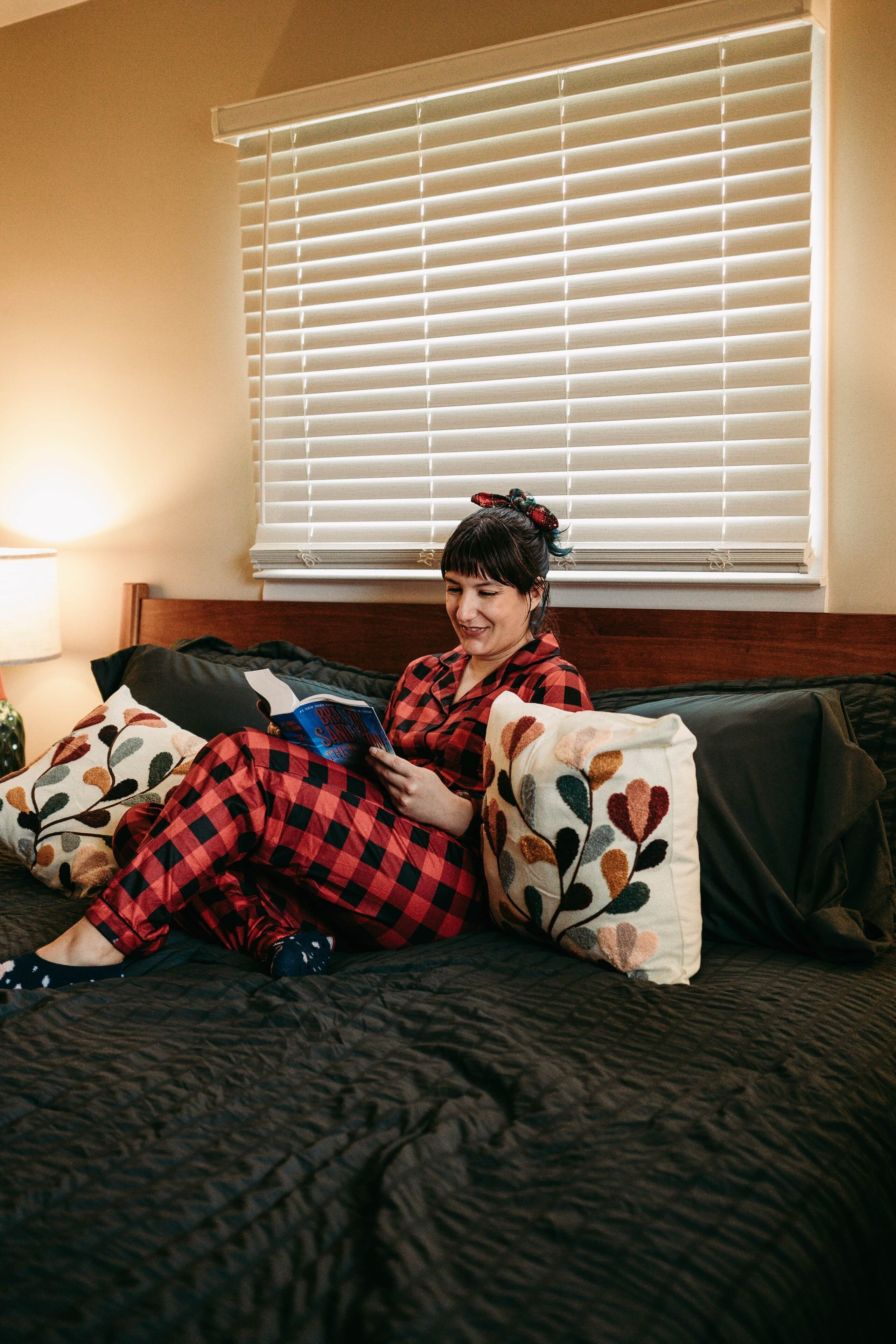 A person sitting on a bed with a dark quilt, reading a book.
