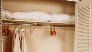 A bedroom with a bed, a closet with hanging clothes, a laundry basket, and a wooden bench. - Retro Rewind (Birch Run)
