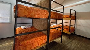Køjesenge med orange sengetøj i et rum med trægulv og hvide vægge.
