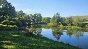 A calm lake surrounded by lush greenery and trees. - eMkhosini Royal Sun (Underberg)