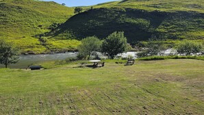 A grassy area with a river, benches, and a picnic table. - eMkhosini Royal Sun (Underberg)