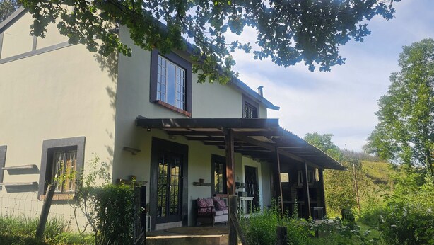 A two-story house with a covered porch, a window with a metal grill, and a door. - eMkhosini Royal Sun (Underberg)