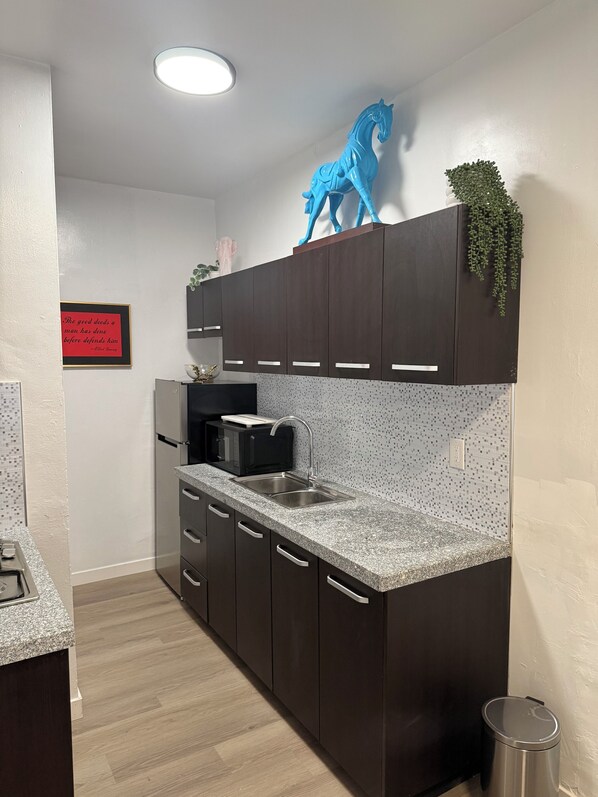 A modern kitchen with dark cabinets, a granite countertop, a toaster, and a blue horse decoration. - Venice Art Studio Apartment (Los Angeles)