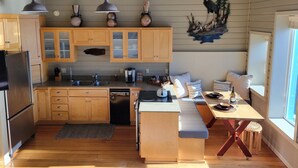 A compact kitchen with wooden cabinets, a built-in dishwasher, and a dining area with a bench and stools. - The Lockers ~ Waterfront ~ Historic Old Town (Florence)