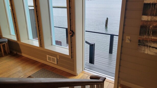 A room with large windows overlooking a lake, a wooden deck outside, and a view of a forested area. - The Lockers ~ Waterfront ~ Historic Old Town (Florence)
