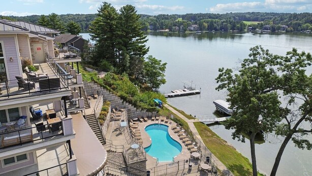A residential building with a swimming pool, outdoor seating, and a view of a lake with boats. - Water`s Edge Luxury Retreat at Delton Grand (Wisconsin Dells)