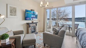 A modern living room with a fireplace, a flat-screen TV, and a large window overlooking a lake. - Water`s Edge Luxury Retreat at Delton Grand (Wisconsin Dells)