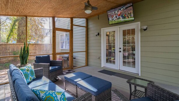 A covered patio with wicker furniture, a television mounted on the wall, and a view of the backyard. - Greensboro`s Gem! Group Friendly, Central Location (Greensboro)