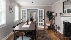 A dining room with a long table, chairs, a fireplace, and a view into another room. - Greensboro`s Gem! Group Friendly, Central Location (Greensboro)
