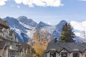 A mountain backdrop with residential buildings featuring balconies and a tree with autumn leaves. - Cozy Canmore 2-Bedroom Retreat (Canmore)