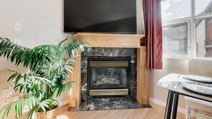 Un saló amb una llar de foc, un televisor de pantalla plana muntat a la part superior, una taula de dinar amb cadires i una planta gran en test.