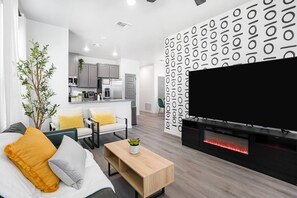 Ein modernes Wohnzimmer mit Flachbildfernseher, einer Couch, einem Couchtisch und einem Essbereich mit Stühlen.