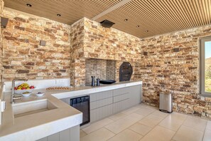A kitchen with a stone wall backsplash, a built-in oven, and a modern countertop. - Villa Raphael - Luxury and Serenity in Paros (Naousa)
