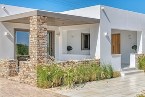A modern house with a stone pillar, large windows, and a tiled patio. - Villa Raphael - Luxury and Serenity in Paros (Naousa)