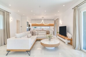 A modern living room with a sofa, coffee table, and TV. - Villa Raphael - Luxury and Serenity in Paros (Naousa)