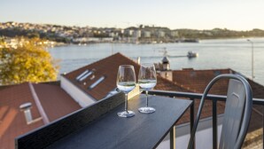 Zwei Gläser Weißwein auf einem Balkon mit Blick auf einen Hafen und Gebäude im Hintergrund.