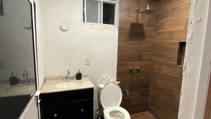 Bany amb vàter blanc, un lavabo i una zona de banyera amb parets de fusta.