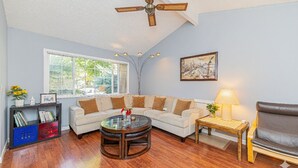A living room with a sectional sofa, a round coffee table, a bookshelf, a side table with a lamp, and a ceiling fan. - Family and Business Friendly Home near Great Mall & BART - 2640 (San Jose)