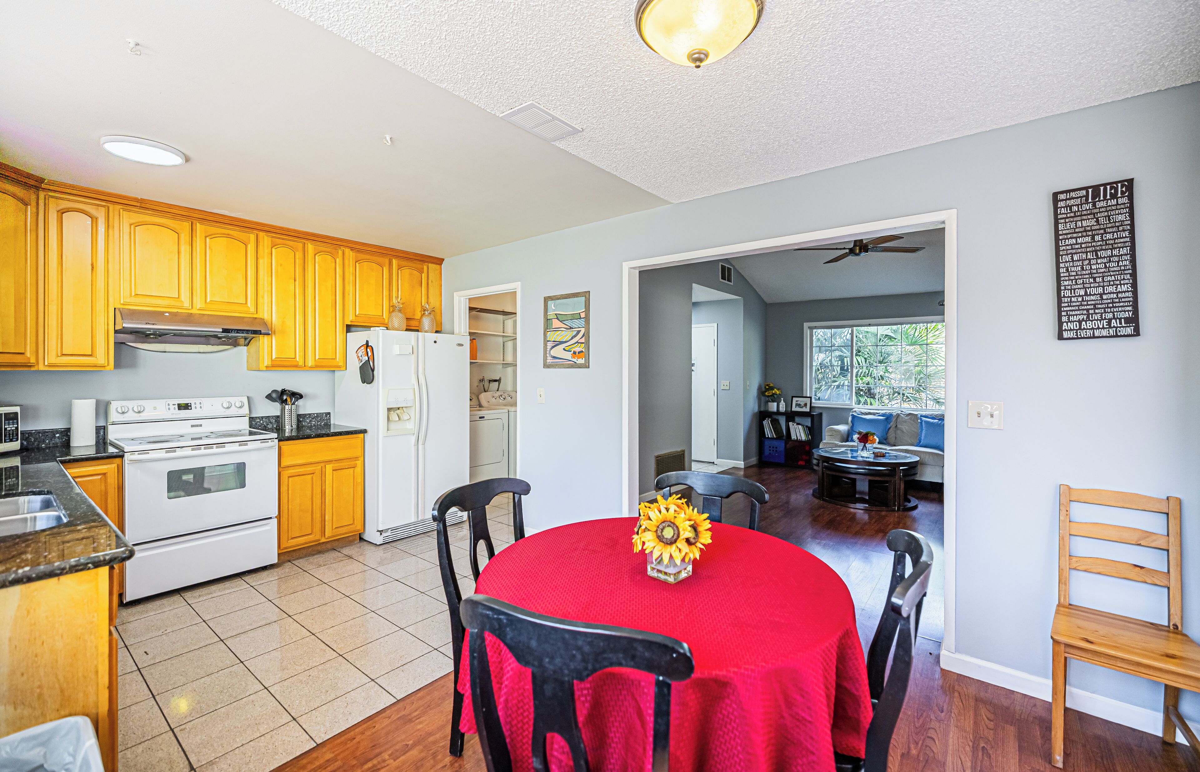 A kitchen with wooden cabinets, a stove, and a dining area with a red tablecloth and chairs.