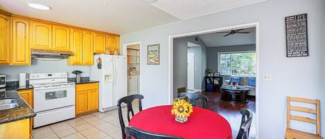A kitchen with wooden cabinets, a stove, and a dining area with a red tablecloth and chairs.